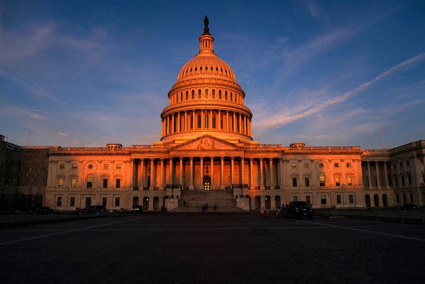 The West Front of the neoclassical US Capitol in Washington is bathed in morning sun up against a blue sky.