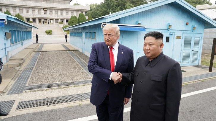 Donald Trump looks to the left and purses his lips as he clutches Kim Jong-un's hand.