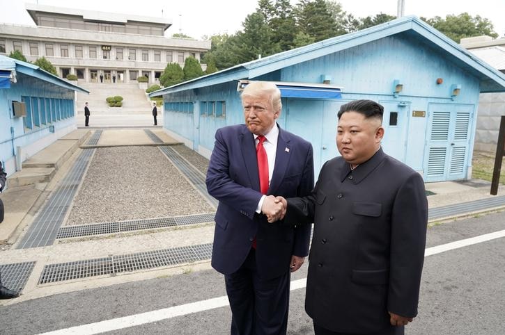 도널드 트럼프가 김정은의 손을 잡고 입술을 오므리고 왼쪽을 바라보고 있다.