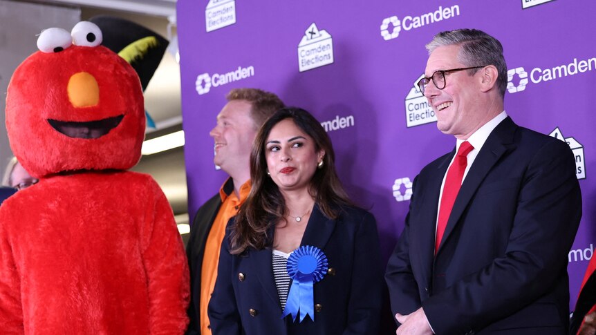 Keir Starmer stands on a stage with other candidates, one of whom is wearing an elmo costume.