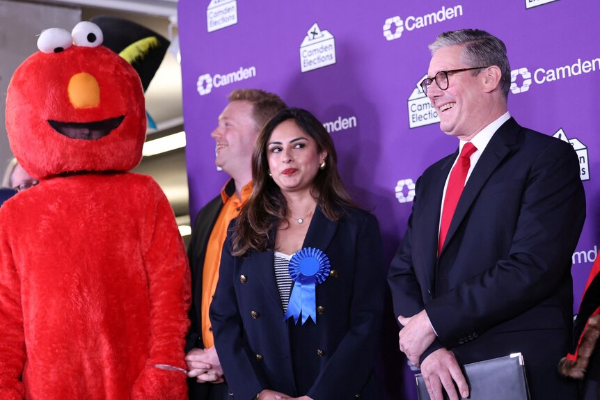 Keir Starmer stands on a stage with other candidates, one of whom is wearing an elmo costume.