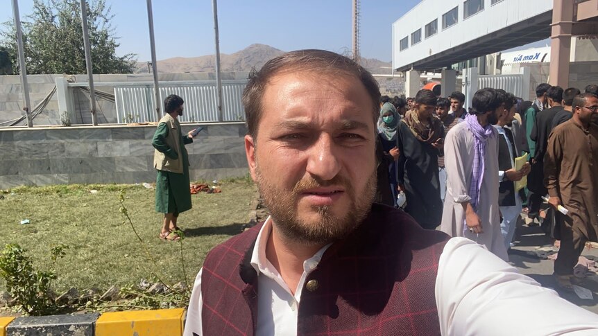 Muftahudin takes a selfie at the Kabul airport with people behind him.