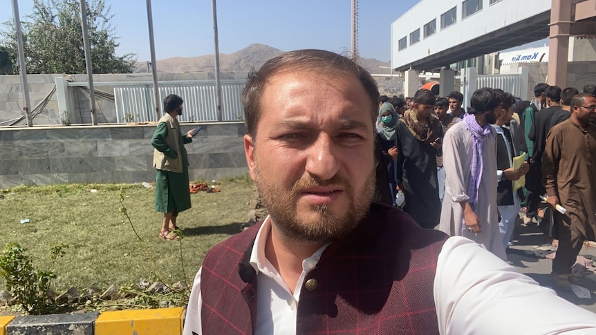 Muftahudin takes a selfie at the Kabul airport with people behind him.