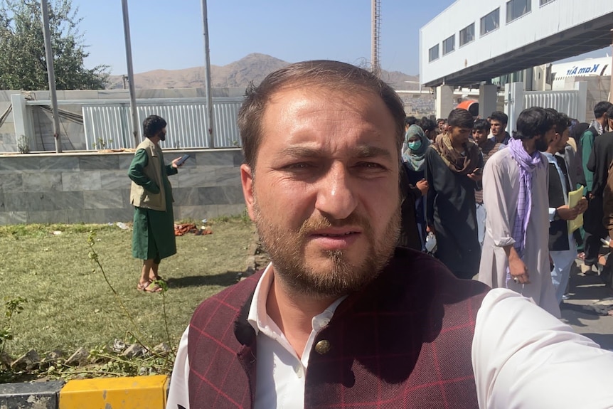 Muftahudin takes a selfie at the Kabul airport with people behind him.