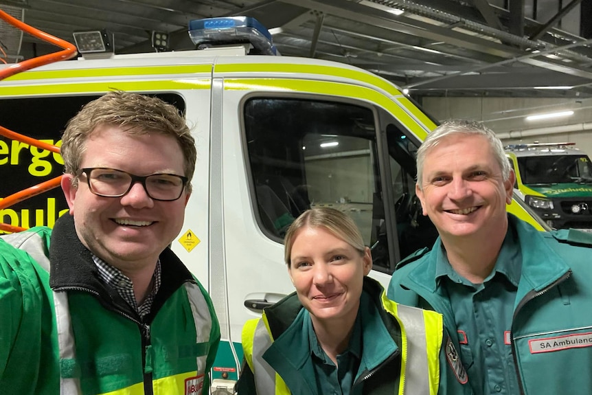 A close up of two men and a woman wearing green ambulance uniforms in front of an ambulance
