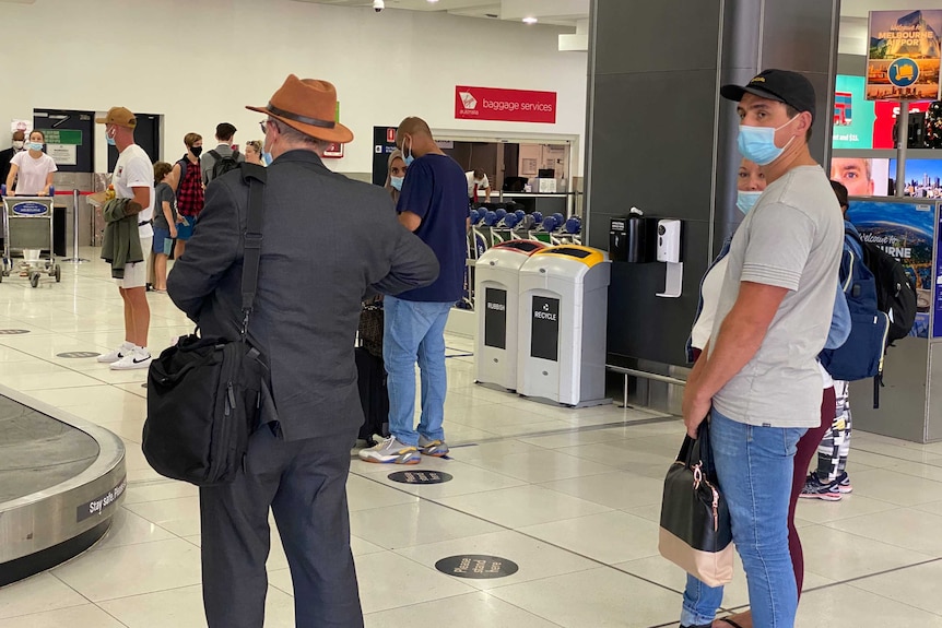People in protective masks stand around waiting for their bags at Melbourne airport.
