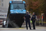 Police stand near the bus which has fallen into a sinkhole
