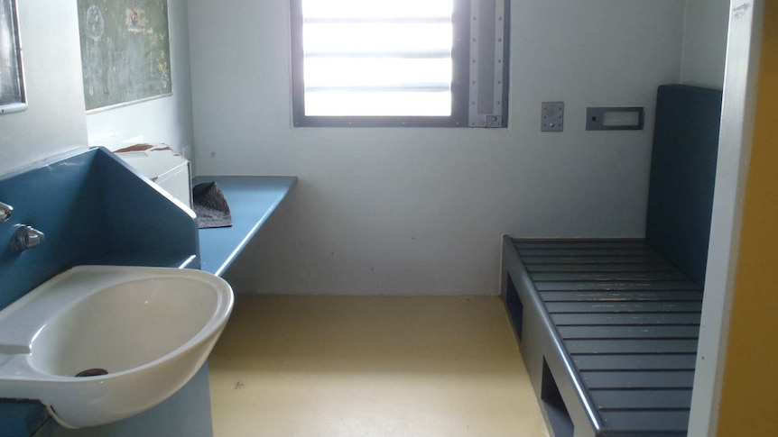 A prison cell is shown including a basin, a window, a desk and space for a bed.