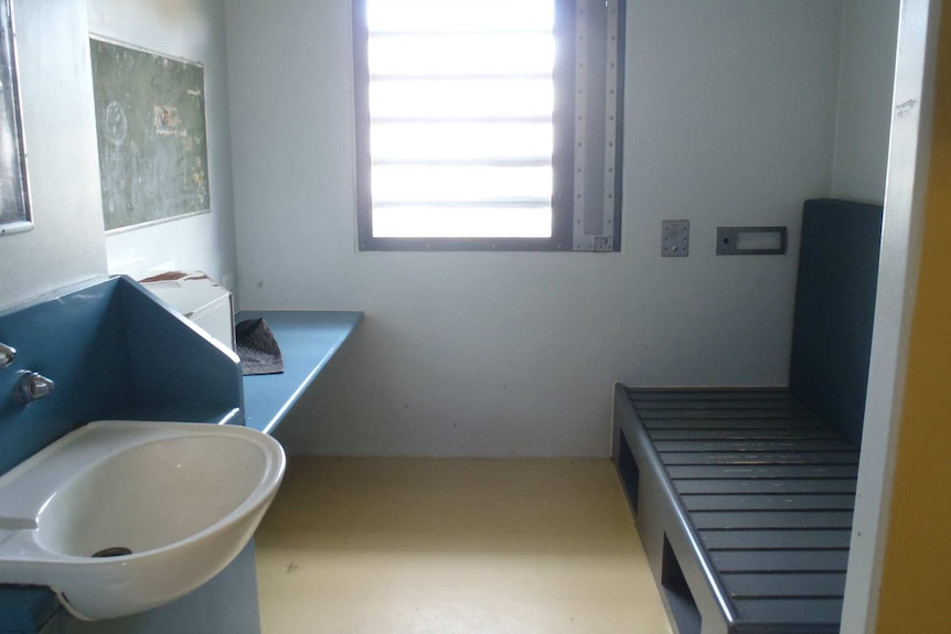 A prison cell is shown including a basin, a window, a desk and space for a bed.