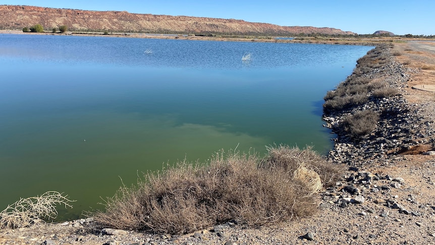 A view of a blue lake, set in an arid landscape, with mountain ranges in the background