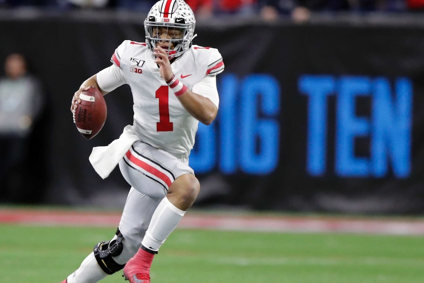 An American football players runs while carrying the ball and looking upfield