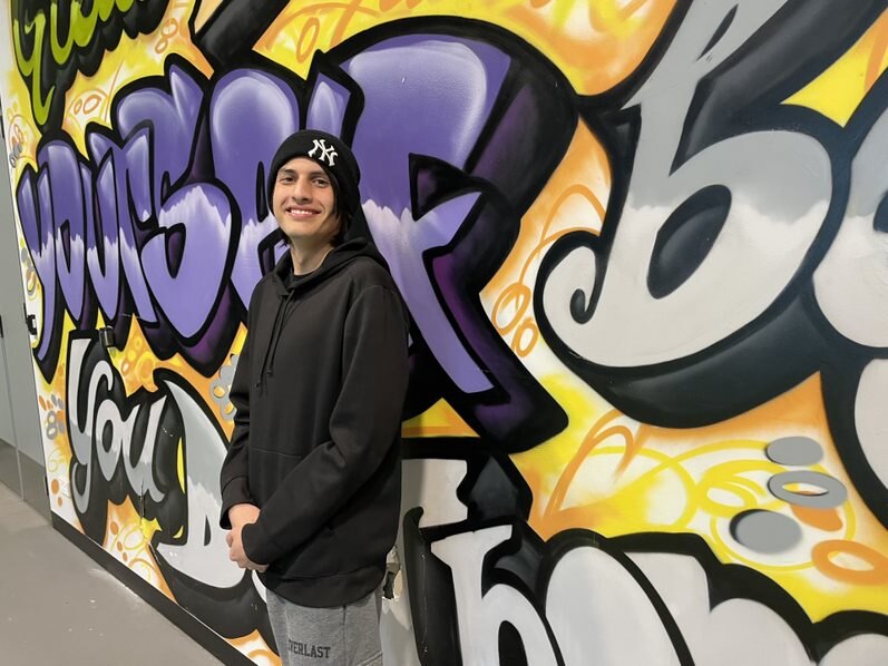 Sam stands in front of a wall with encouraging words painted on it.