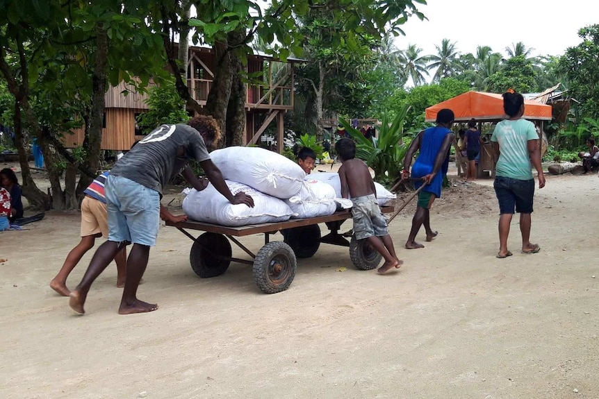 Locals including children work together to push a buggy loaded with sacks of goods.