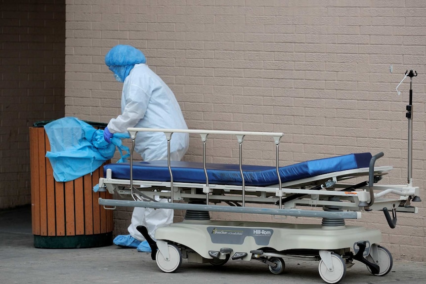 a worker places protective clothing into a garbage can outside a medical centre
