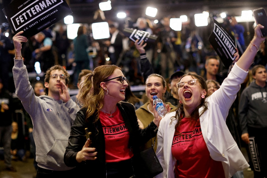 Two women holding "John Fetterman" signs smiling and laughing