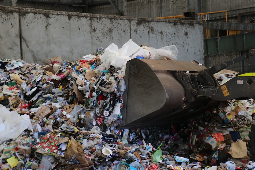 A forklift scoops a large pile of recyclable material such as plastic bottles at a recycling facility.