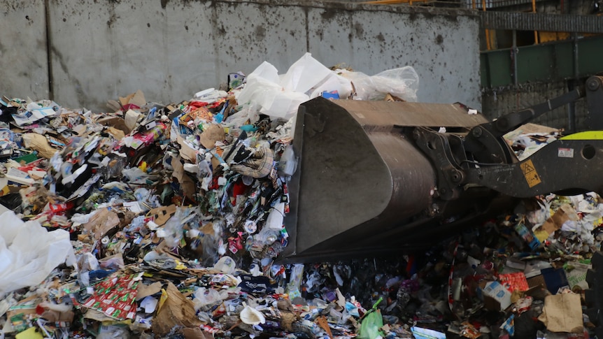 A forklift scoops a large pile of recyclable material such as plastic bottles at a recycling facility.