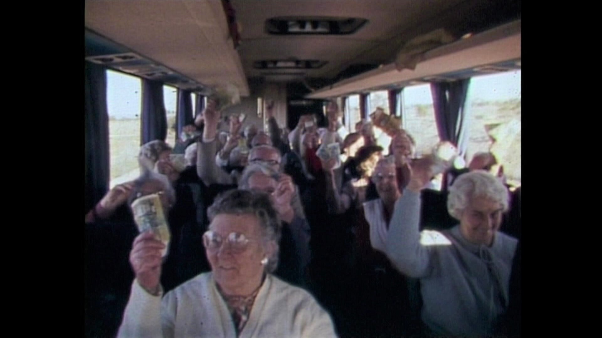 A bus full of older people wave money in the air.