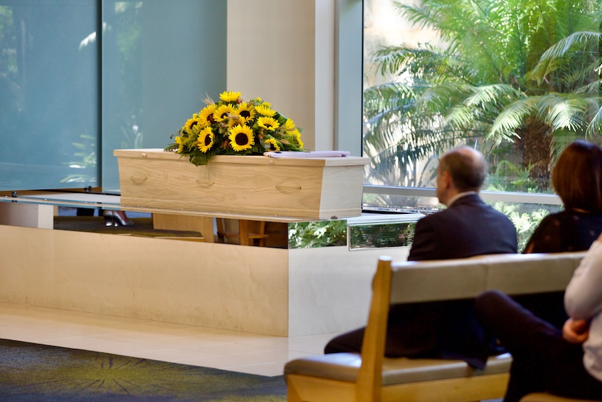 A bouquet of sunflowers on a pine coffin at a funeral service