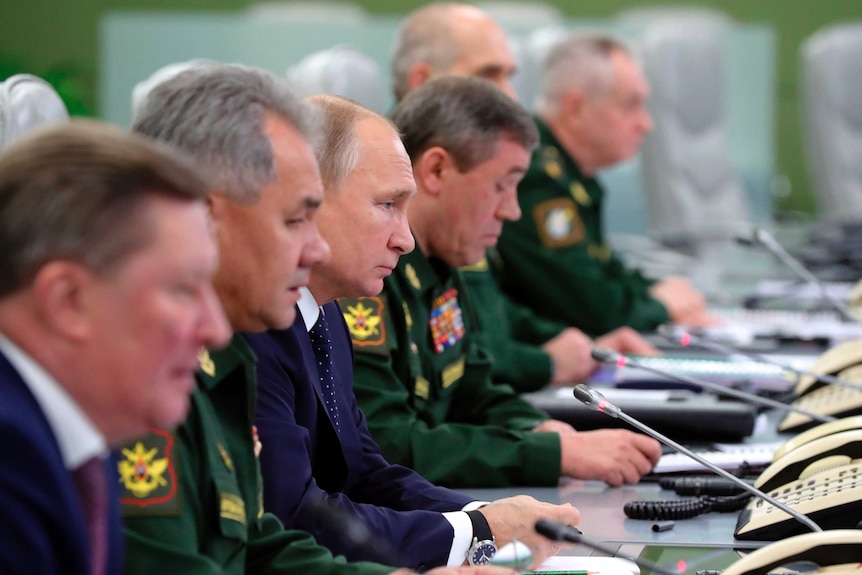 Russian officials sit in a row to watch the weapon test with Putin in the centre.