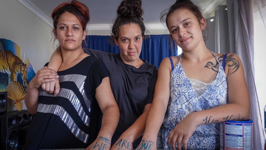 Three women with their fists on a bench with the words "we are one" on their skin.