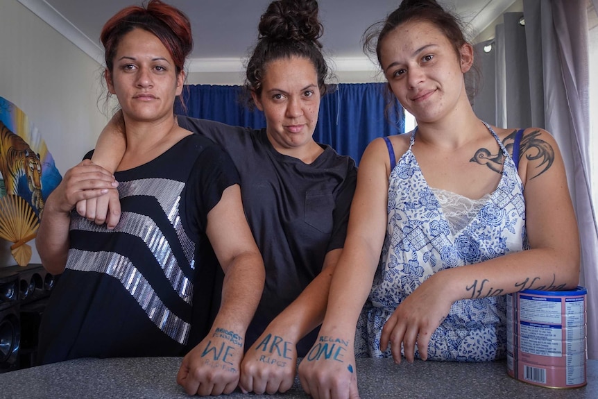 Three women with their fists on a bench with the words "we are one" on their skin.