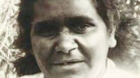 Close up headshot of Indigenous woman in a white shirt, trees in background