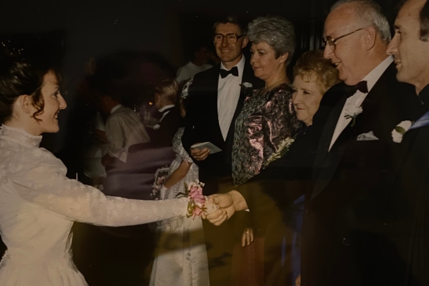 A photo of a woman in a white dress reaching out to two men wearing suits.