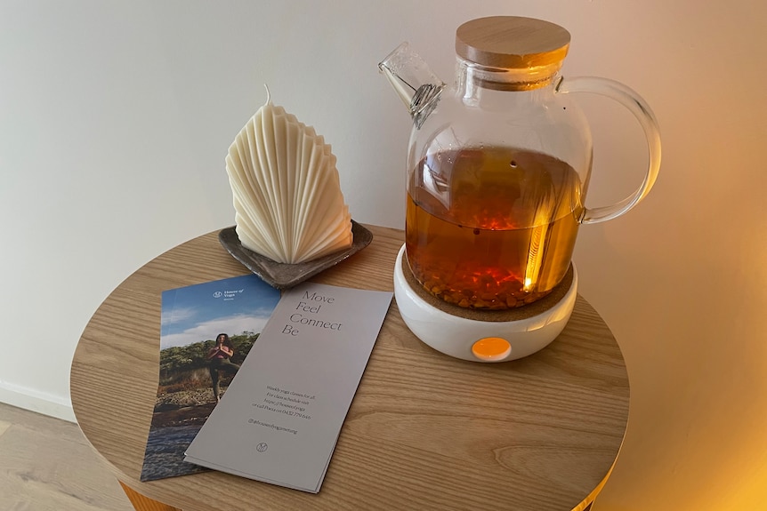 A glass herbal tea pot sits on a round, wooden table.