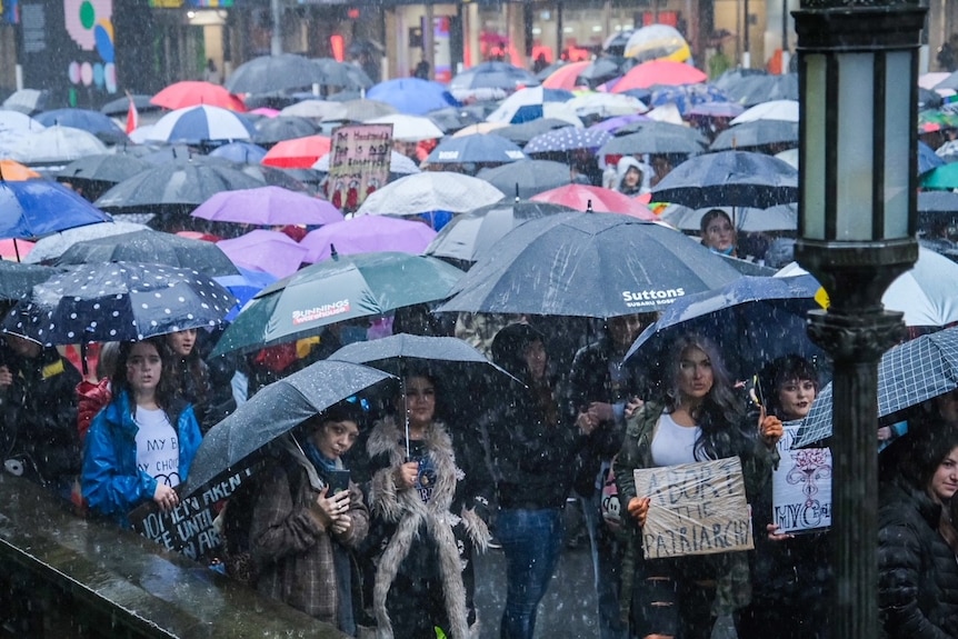 Una folla in piedi sotto un cielo cupo e piove con gli ombrelli.