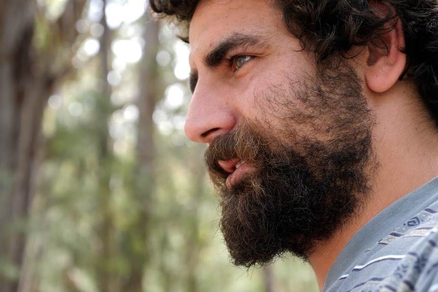 Close up of young man with beard looking intently, forest in background