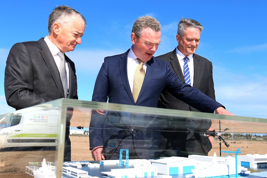 Three ministers look at a model of a shipbuilding facility.