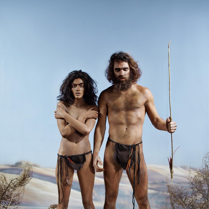 Prehistoric woman stands next to a man holding a spear