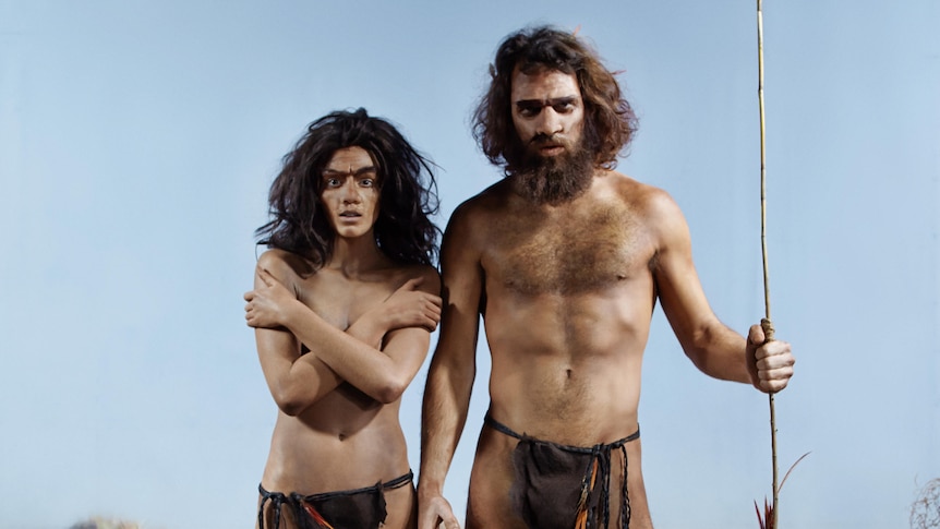 Prehistoric woman stands next to a man holding a spear