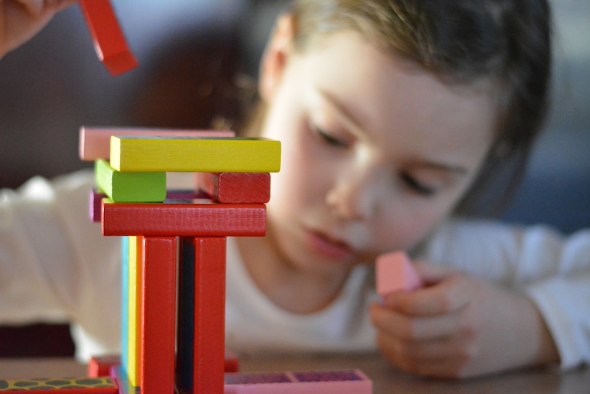A child stacks colourful building blocks on a table.