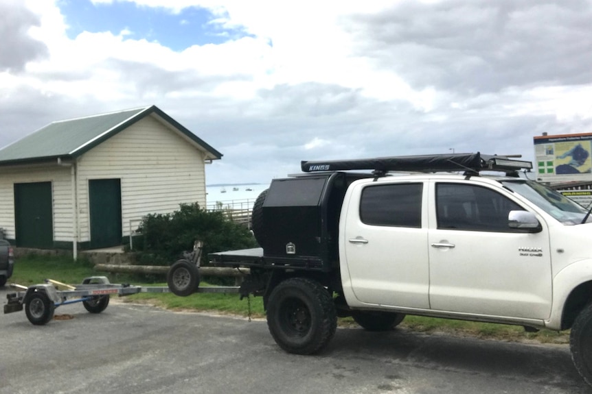 A white utility with a trailer attached is parked outside a small shed at the edge of Westernport Bay.