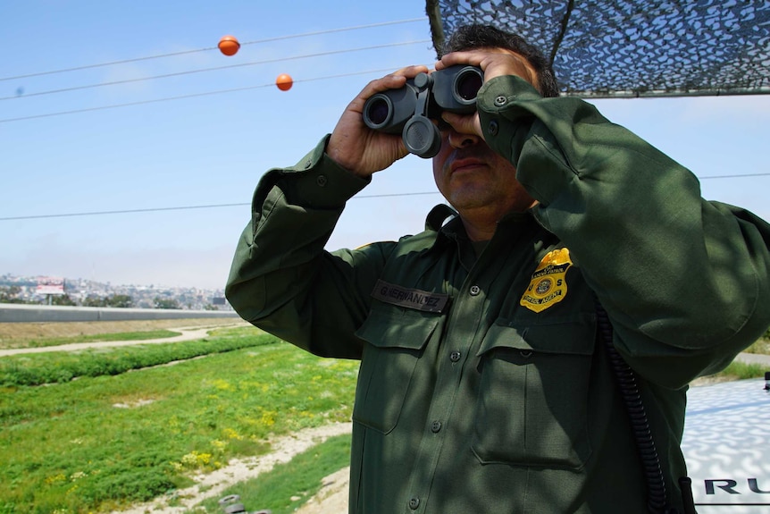 A US Border Patrol agent uses binoculars to watch over the border with Mexico.