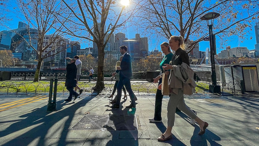 A group of pedestrians walking along a footpath by the Yarra River on a sunny day.