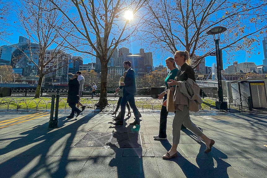 A group of pedestrians walking along a footpath by the Yarra River on a sunny day.