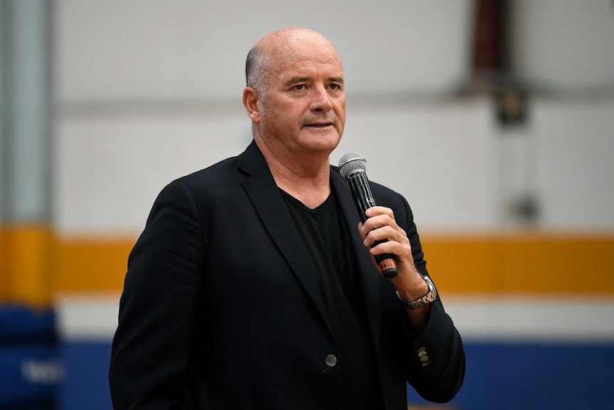 A basketball team owner holds a microphone as he speaks to a crowd.