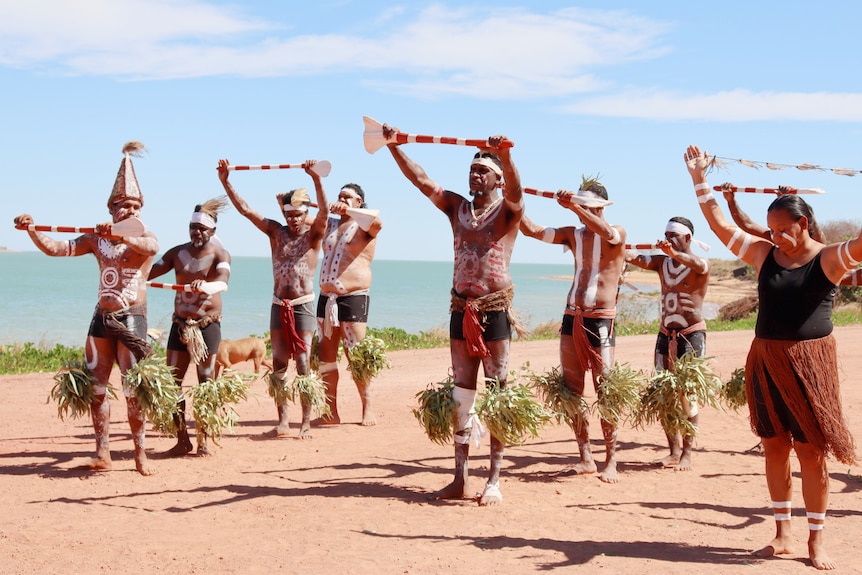 Indigenous dancers in traditional costume dance on a beach