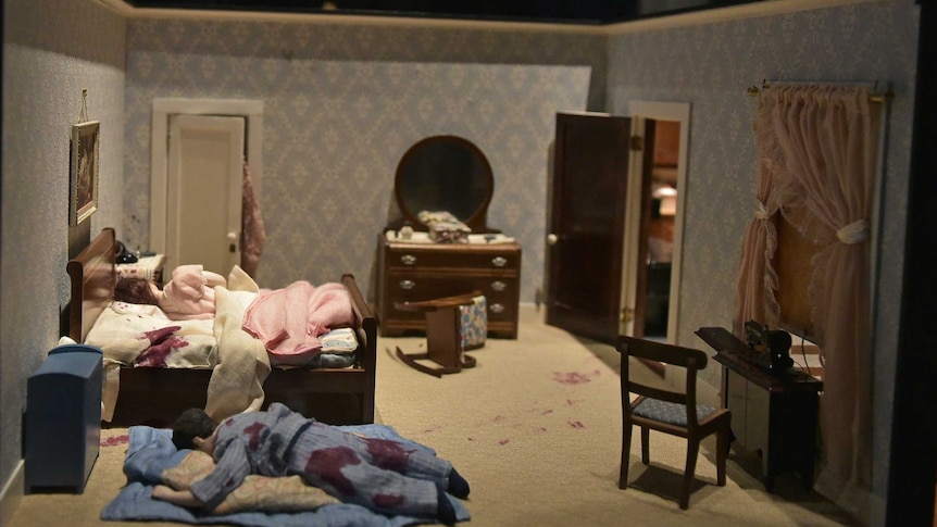 Miniature bedroom in which a man with bloody pyjamas lies face-down on floor and woman with blood near head lies on the bed.