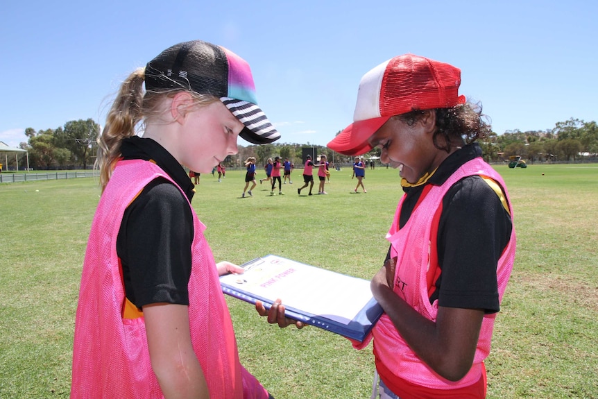 Two girls looking at a clipboard on a football field.