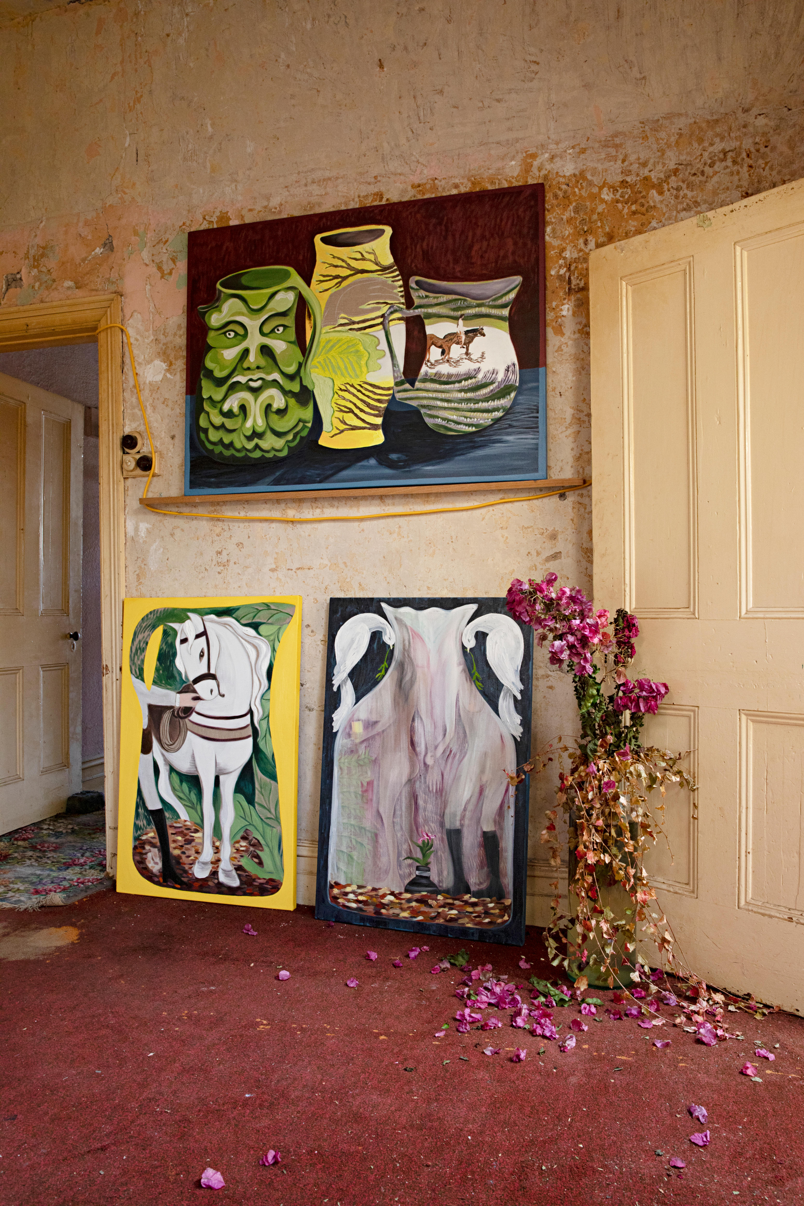 Paintings and dried flowers adorn a wall in a derelict house