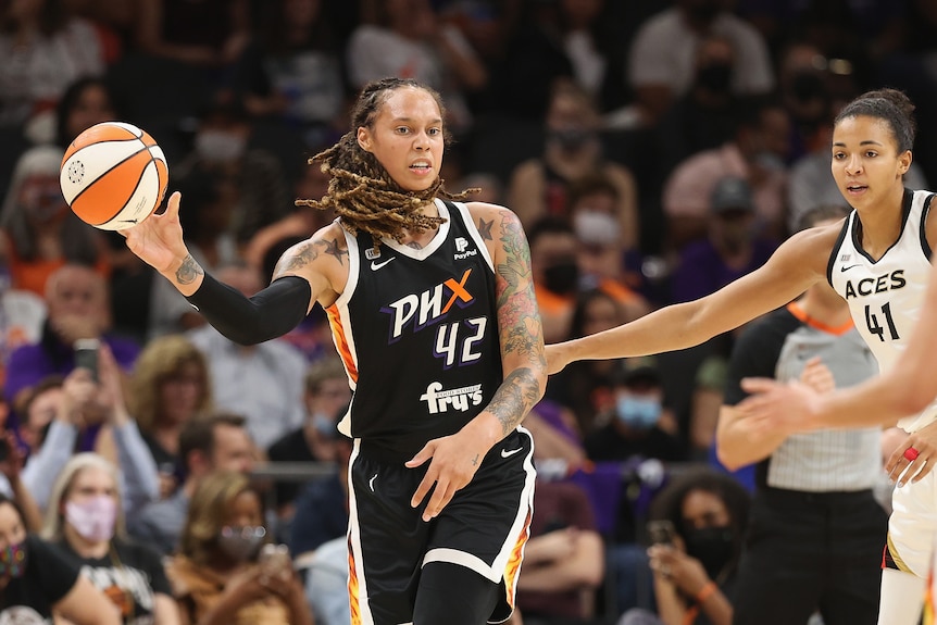 A WNBA player lets the ball go to pass it downcourt as a  defender holds her arm out to try to corral her during a game.