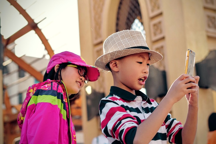 Two young children take a photo with a smartphone.