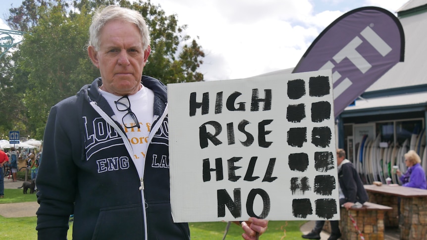 A man standing with a sign that says 'high rise hell no'. 