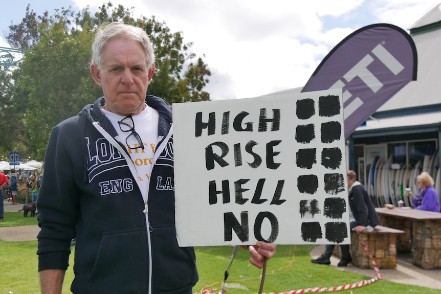 A man standing with a sign that says 'high rise hell no'. 
