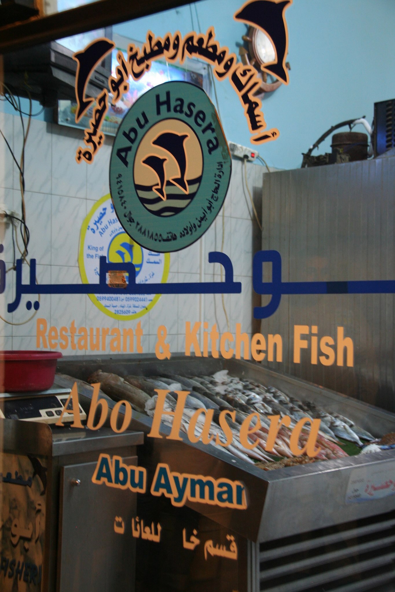 A close up of text stickers acting as a sign on a wall frontage of a fish restaurant. Fish are in a vat beyond the glass.