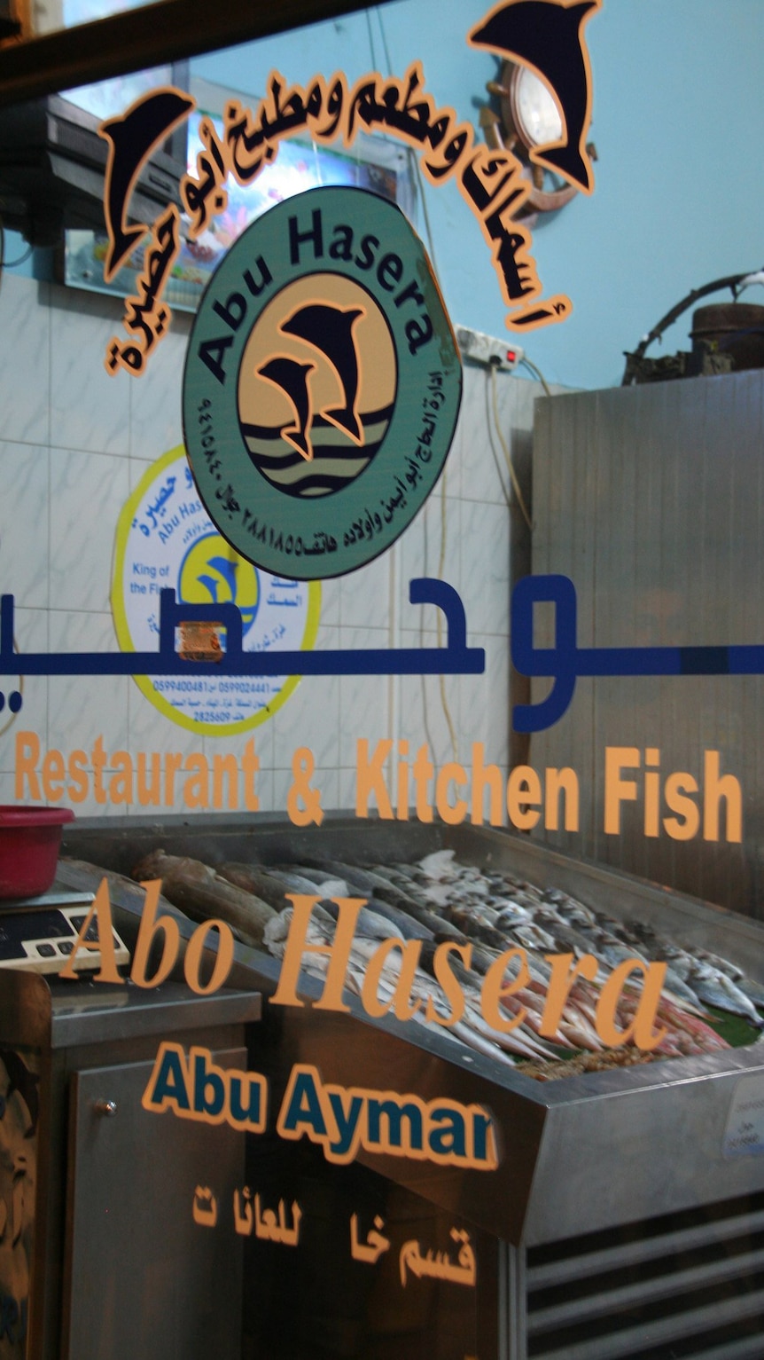 A close up of text stickers acting as a sign on a wall frontage of a fish restaurant. Fish are in a vat beyond the glass.